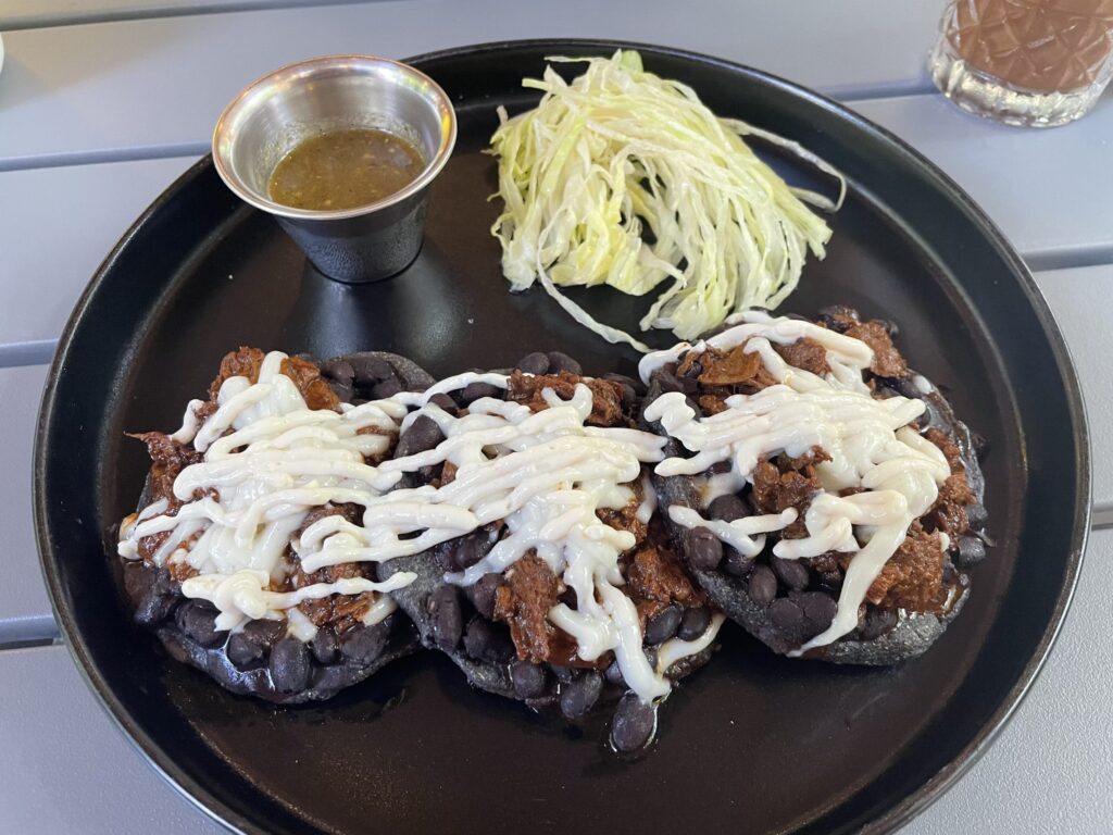 Vegan Los Sopecitos con Pastor – three blue corn sopes with plant-based pastor, beans, lettuce, crema, and red onion